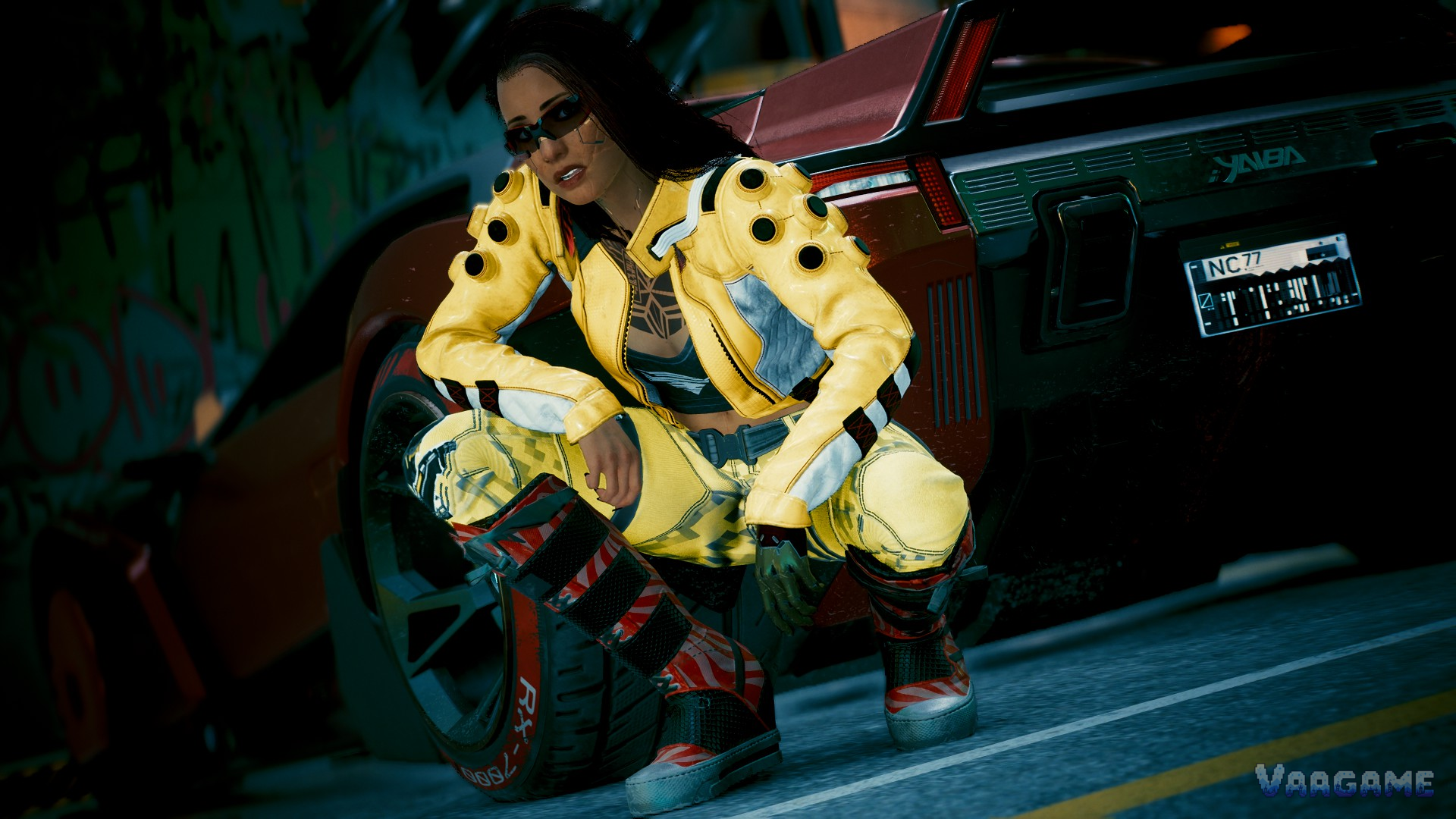 V in a yellow outfit standing beside a sports car at night